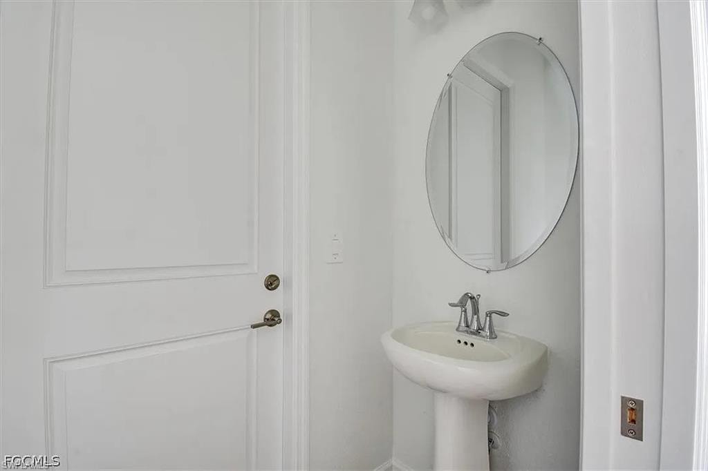 Pedestal sink with chrome faucet, complemented by an oval frameless mirror and white paneled door with brushed nickel hardware