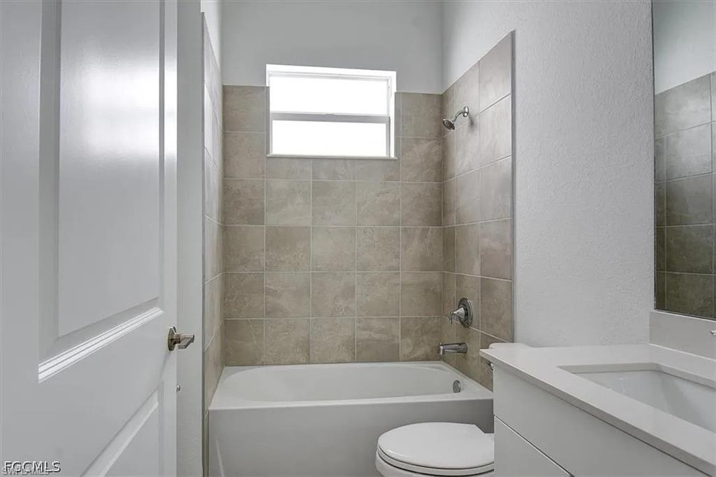 Bathroom featuring a white tub, tiled shower surround, and a white vanity with a rectangular sink