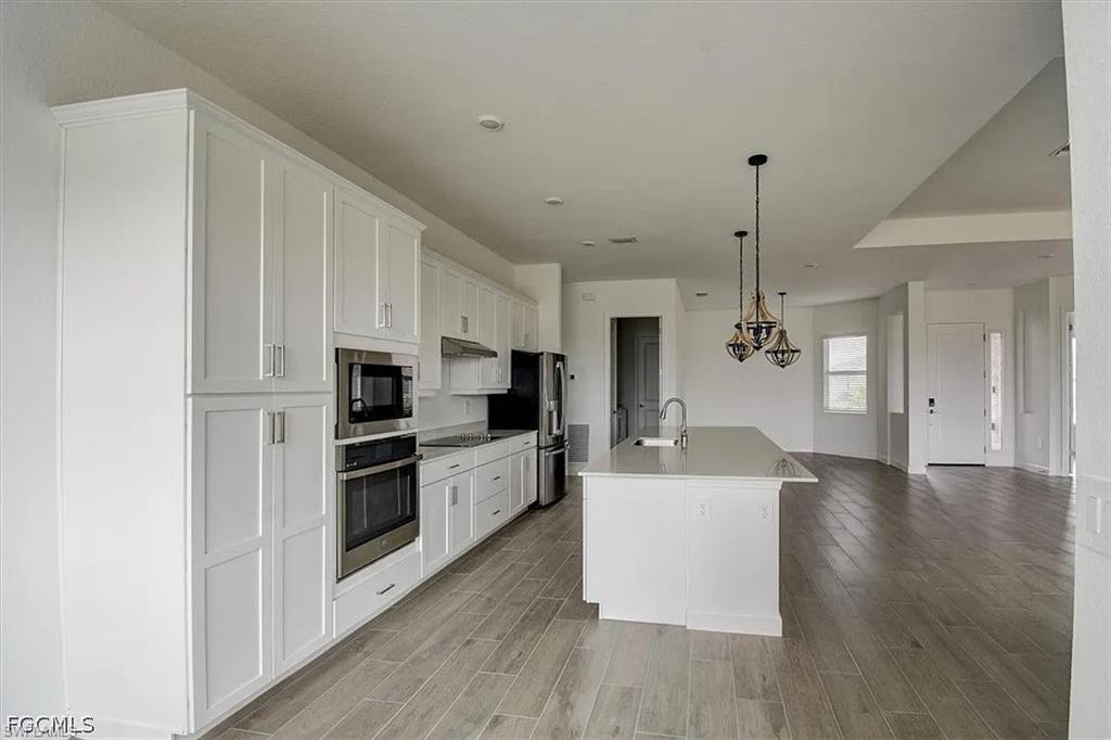 Modern kitchen featuring white cabinetry, stainless steel appliances, a central island with sink, and wood-finish flooring