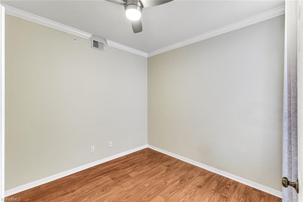 Room with wood-finish flooring, light neutral wall paint, and white crown molding