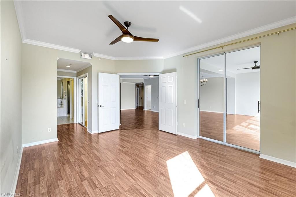 Spacious interior room featuring wood-finish flooring, a ceiling fan with integrated lighting, and crown molding