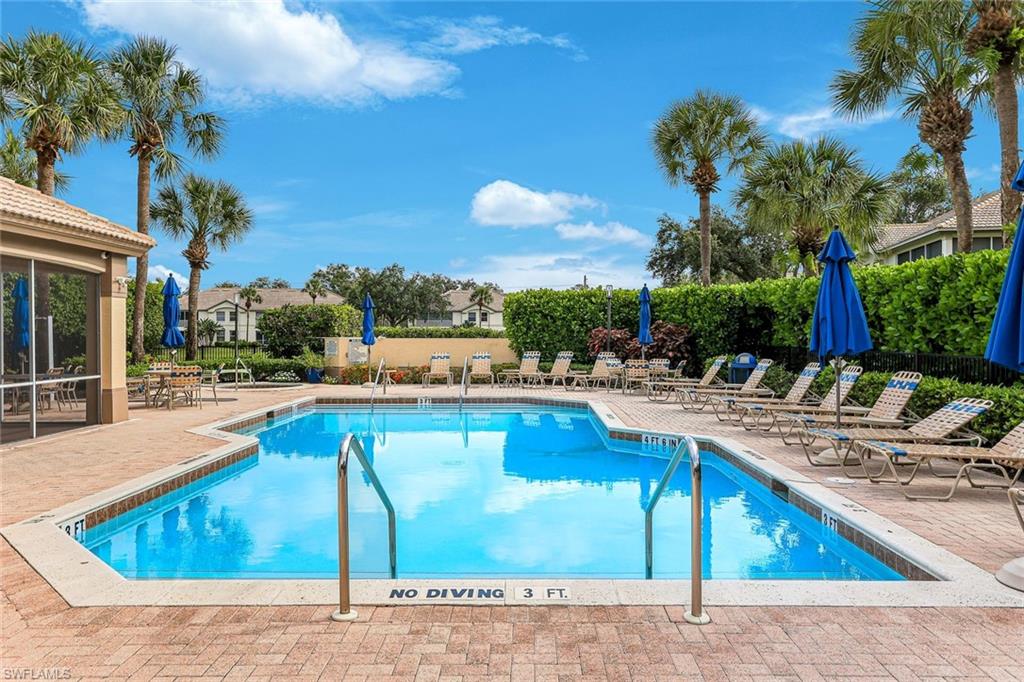 Resort-style swimming pool featuring a brick paver deck, surrounding palm trees, and a screened poolside lounge area