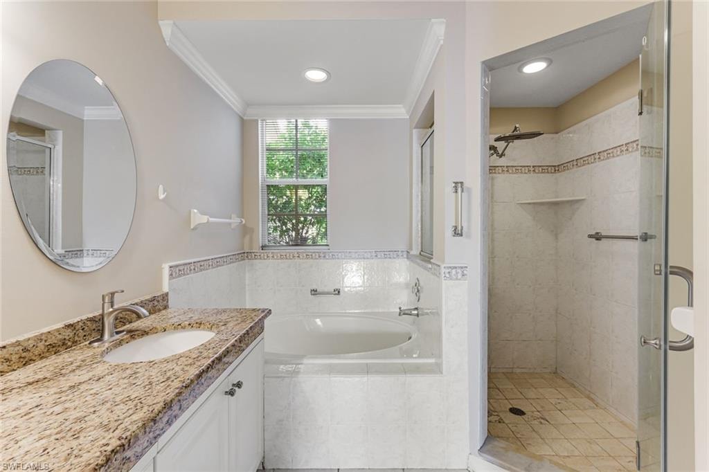 Bathroom featuring a built-in tub, separate glass-enclosed shower, vanity with granite countertop, integrated sink, and an oval mirror