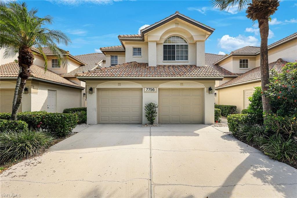 Mediterranean-style exterior featuring a prominent arched window, barrel tile roof, two-car garage, mature landscaping, and palm trees