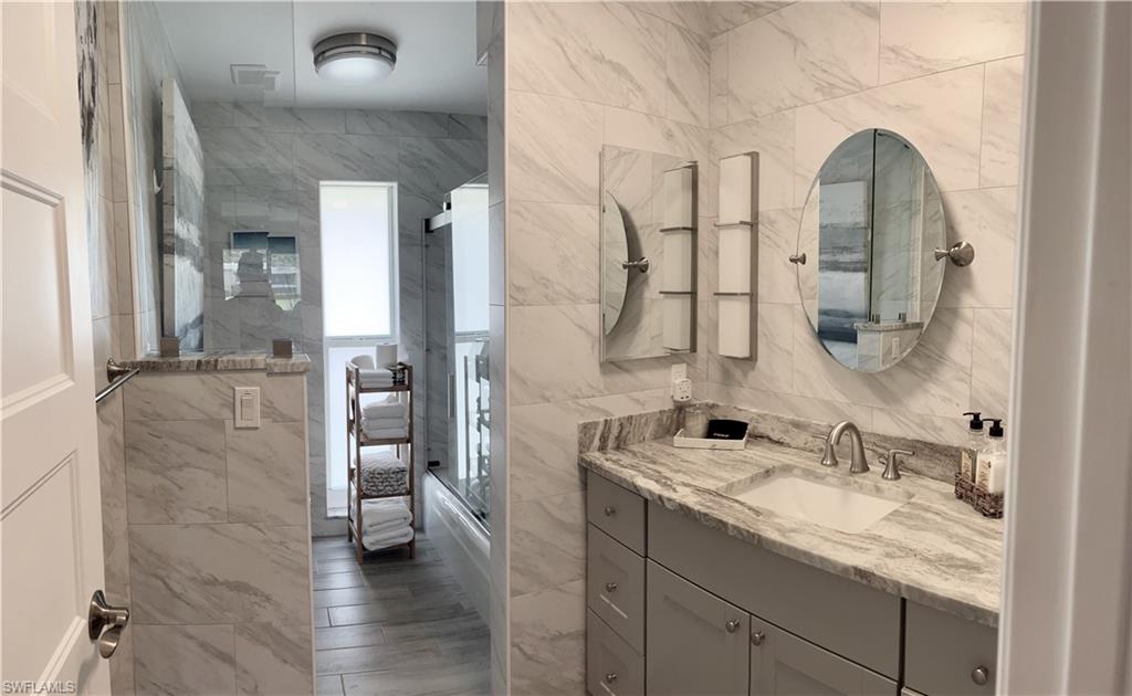 Guest Bathroom with single sink vanity, tile walls, and shower/bath combination with glass door