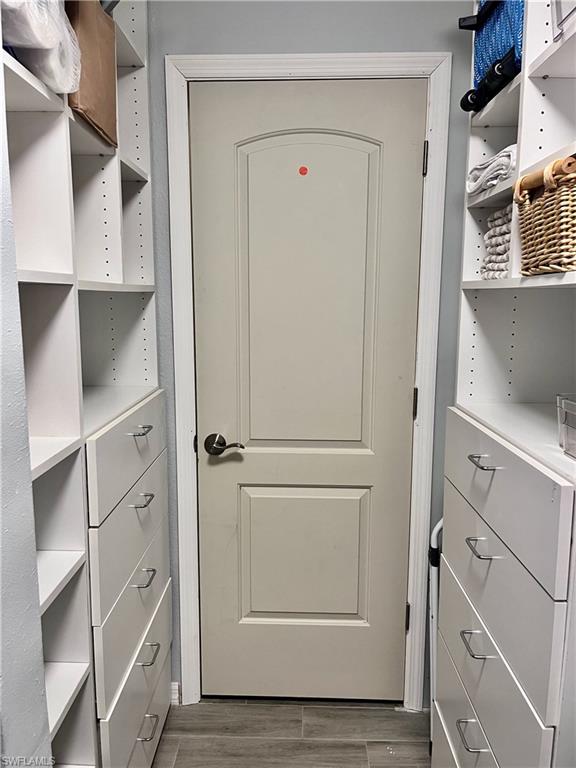 Spacious primary bedroom walk in closet with shelving, drawers and a wood finished floors