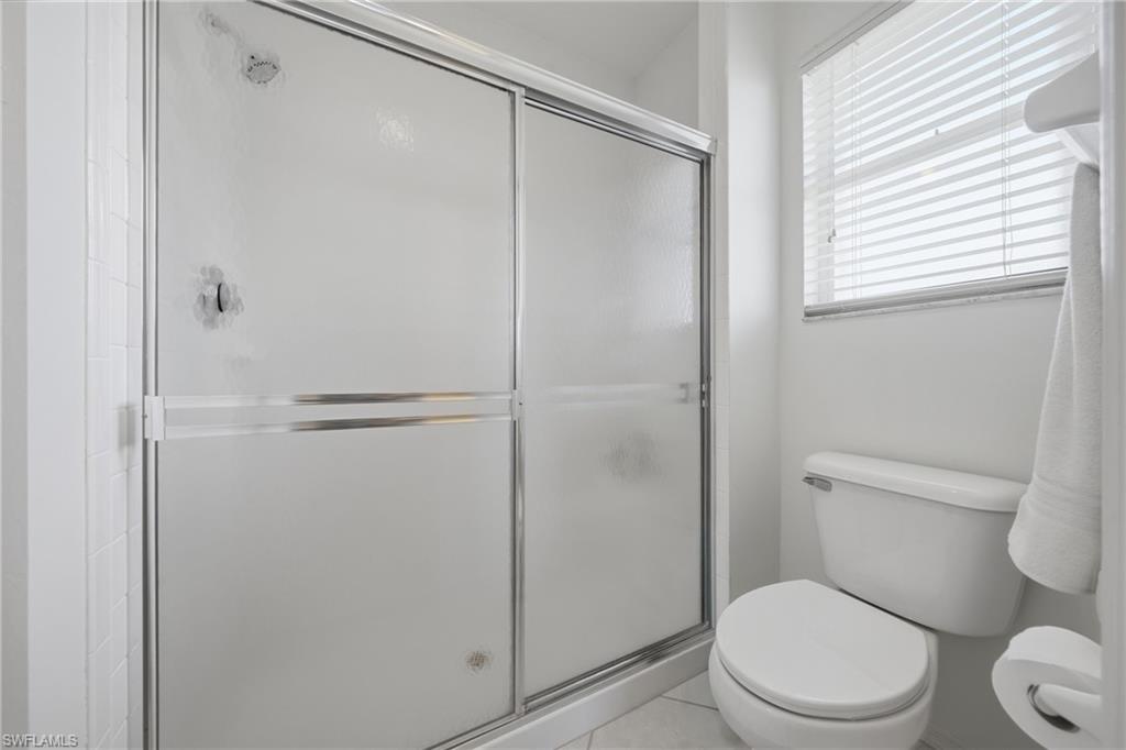 Bathroom featuring a shower with sliding frosted glass doors, white tile surround, white toilet, and a window with blinds