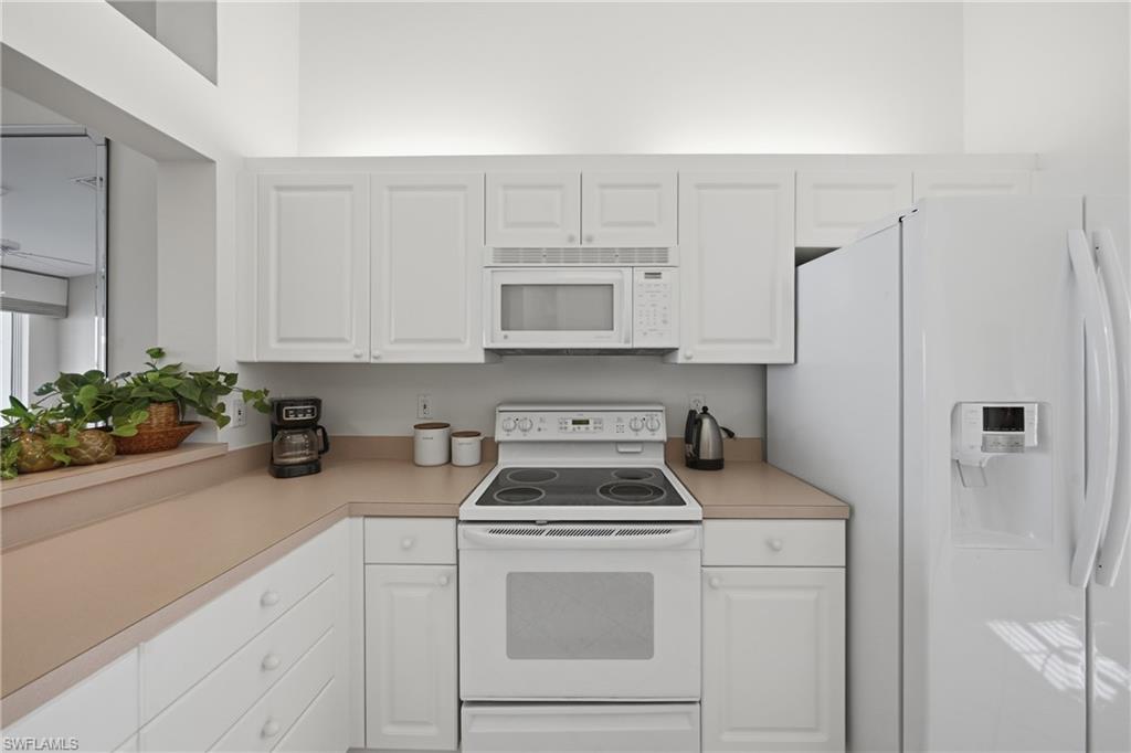 Kitchen featuring white cabinetry with brushed nickel hardware, light-toned countertops, and full-size appliances including a refrigerator with water dispenser, electric range, and built-in microwave
