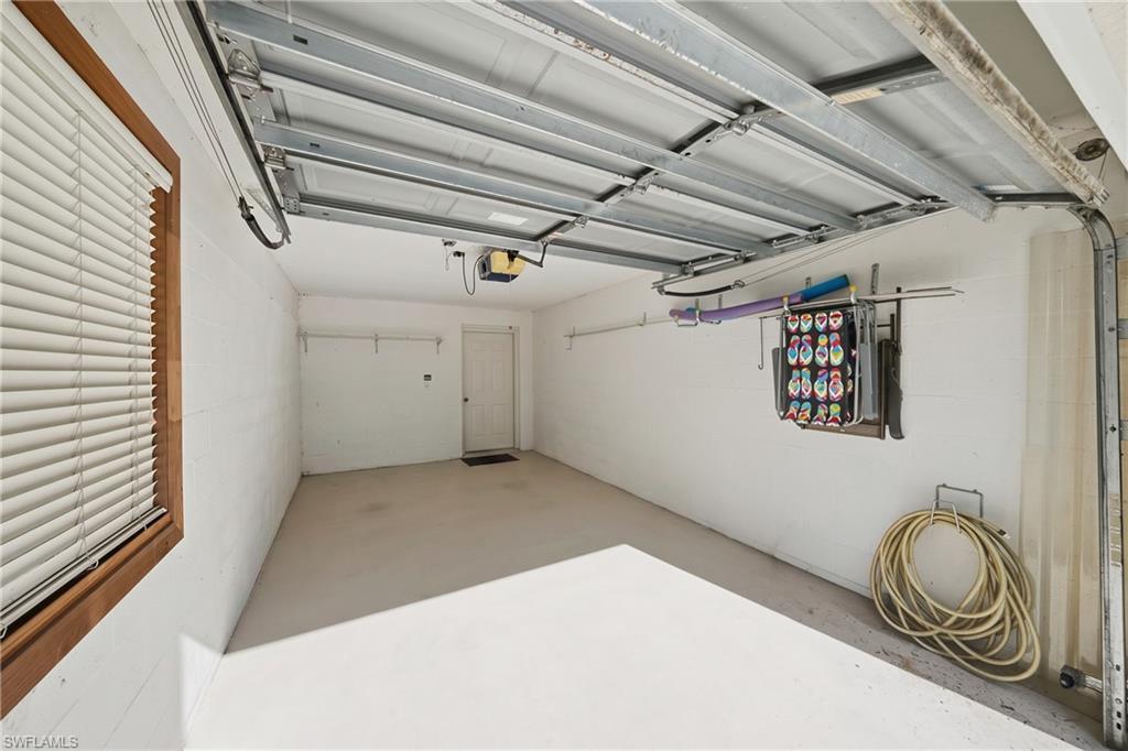 Spacious garage featuring a light-colored concrete floor, white painted walls, a window with wood trim and blinds, a side entry door, and an automatic garage door opener