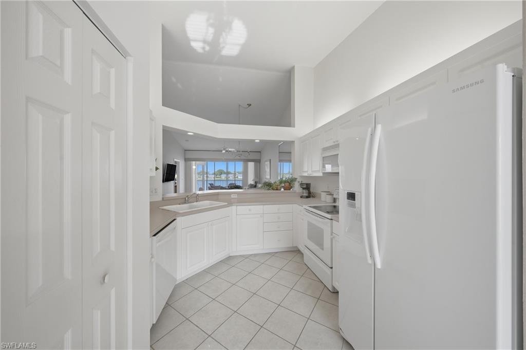 Kitchen featuring white cabinetry, light-toned countertops, white appliances, and tiled flooring