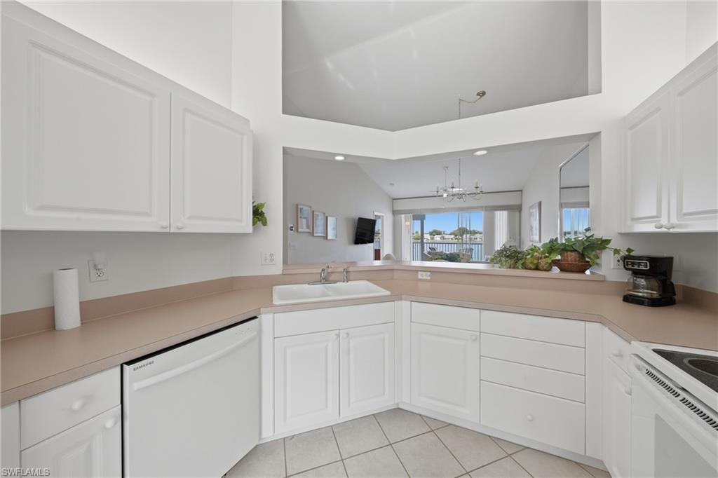 Kitchen featuring white cabinetry, light-toned countertops, a pass-through window, tile flooring, and integrated white appliances
