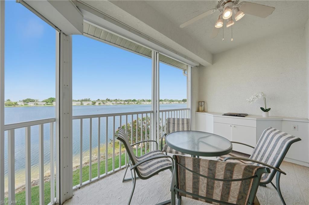 Screened patio with a lake backdrop, featuring a white railing, a white ceiling fan with integrated lighting, and built-in white cabinetry