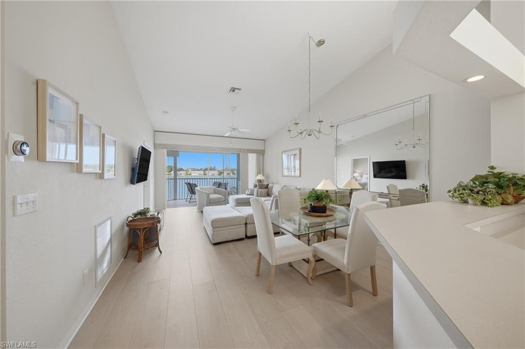 Open-concept living space with vaulted ceilings, wood-finish flooring, a full-wall mirror, and sliding glass doors leading to a balcony