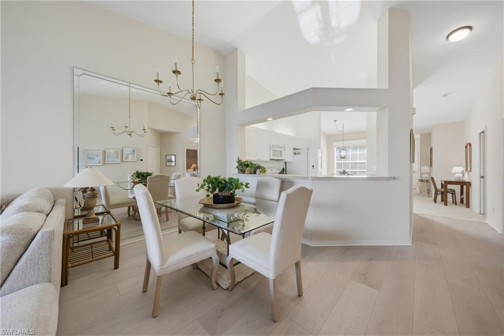 Dining area featuring vaulted ceilings, light wood-finish flooring, and an oversized wall mirror