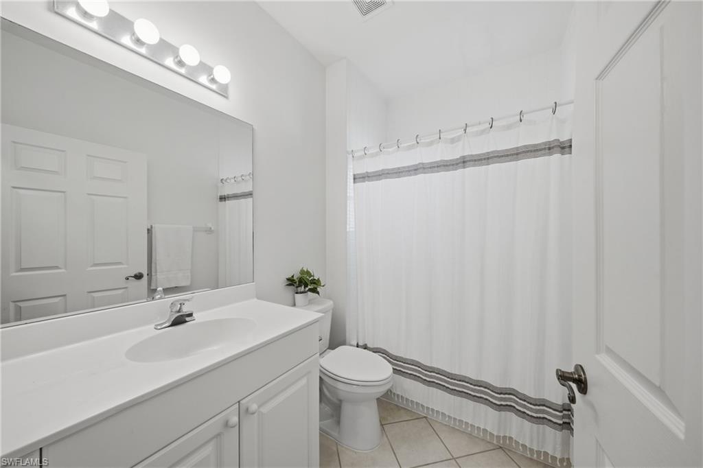 Bathroom featuring a white vanity with integrated sink, a large wall-mounted mirror, overhead bar lighting, a toilet, and tiled flooring