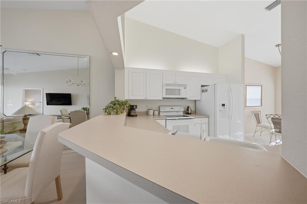 Kitchen featuring a peninsula breakfast bar, white cabinetry, integrated white appliances, and a vaulted ceiling
