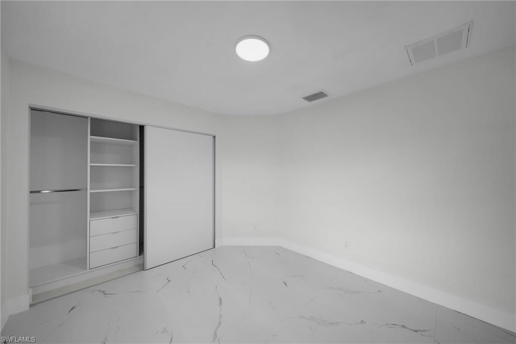 Spacious room featuring wood-finish flooring, a contemporary ceiling light fixture, and a built-in closet system with sliding doors, shelving, and drawers