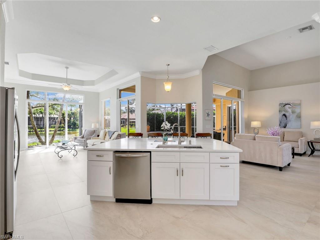 Kitchen with open floor plan, stainless steel appliances, white cabinetry, pendant lighting, and light countertops