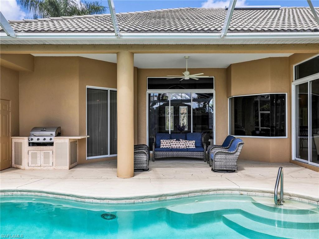 Outdoor pool featuring area for grilling, a patio area, ceiling fan, glass enclosure, and an outdoor living space
