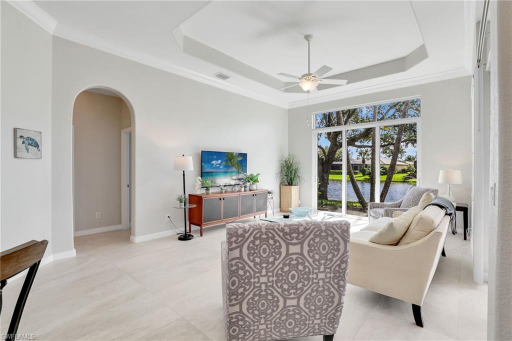 Living area featuring arched walkways, ceiling fan, a raised ceiling, and crown molding