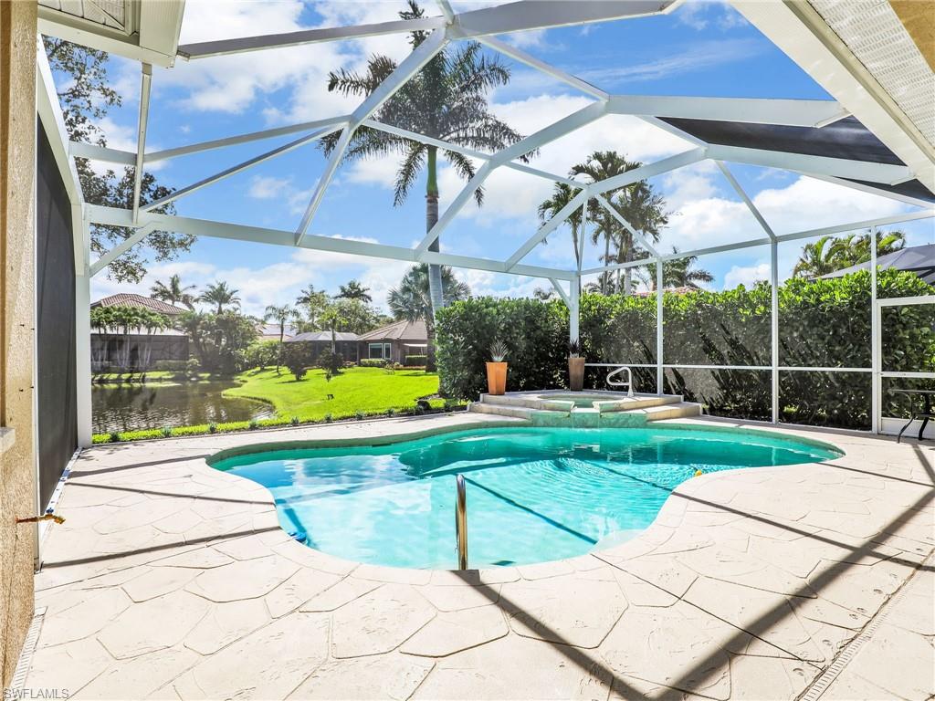 View of pool featuring a patio area, a yard, a pool with connected hot tub, and glass enclosure