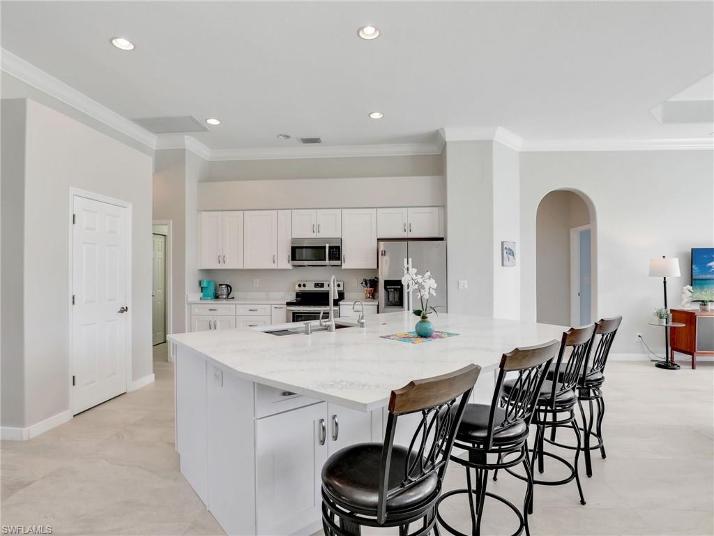 Kitchen featuring stainless steel appliances, ornamental molding, arched walkways, white cabinetry, and a large island