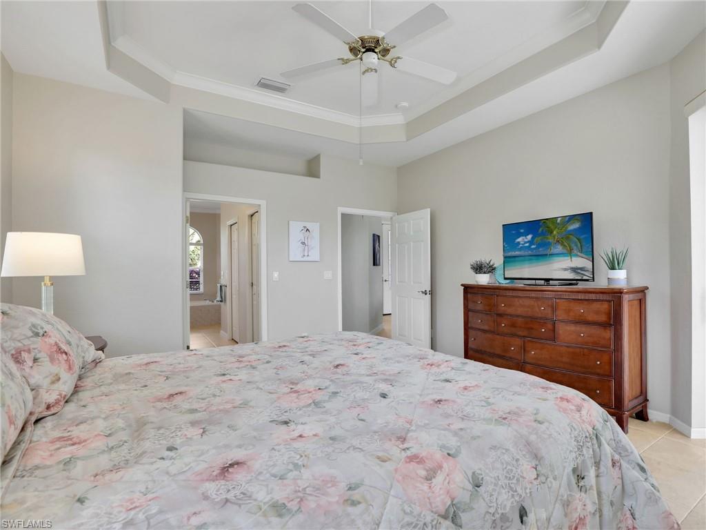 Bedroom with light tile patterned floors, ornamental molding, a tray ceiling, and ceiling fan