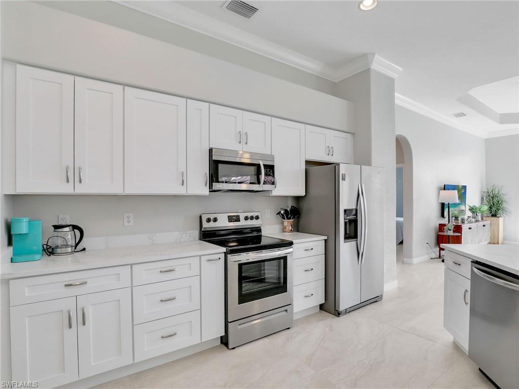 Kitchen featuring stainless steel appliances, ornamental molding, arched walkways, and white cabinetry