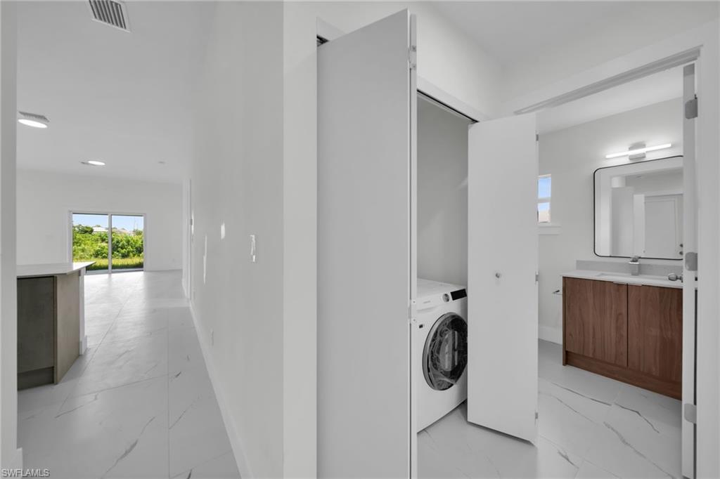 Integrated laundry closet with bi-fold doors, modern bathroom vanity with wood-finish cabinetry, quartz countertop, and rectangular mirror
