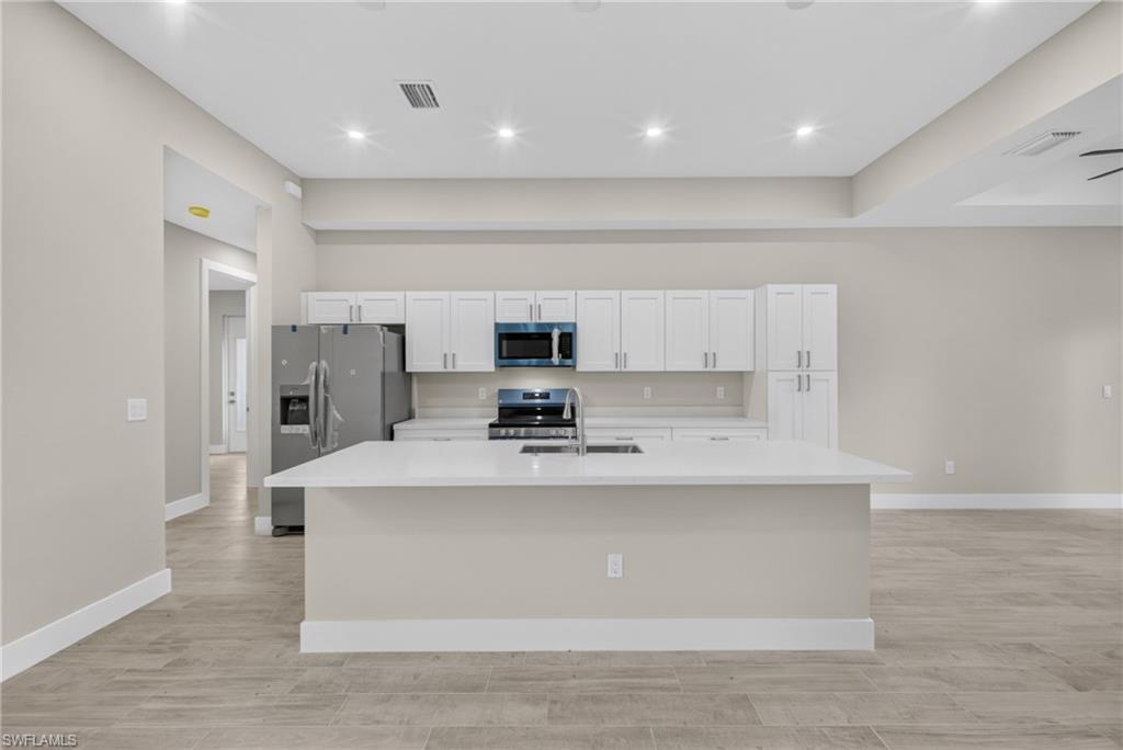 Kitchen featuring a central island with an undermount sink, white cabinetry, light-toned countertops, and recessed lighting