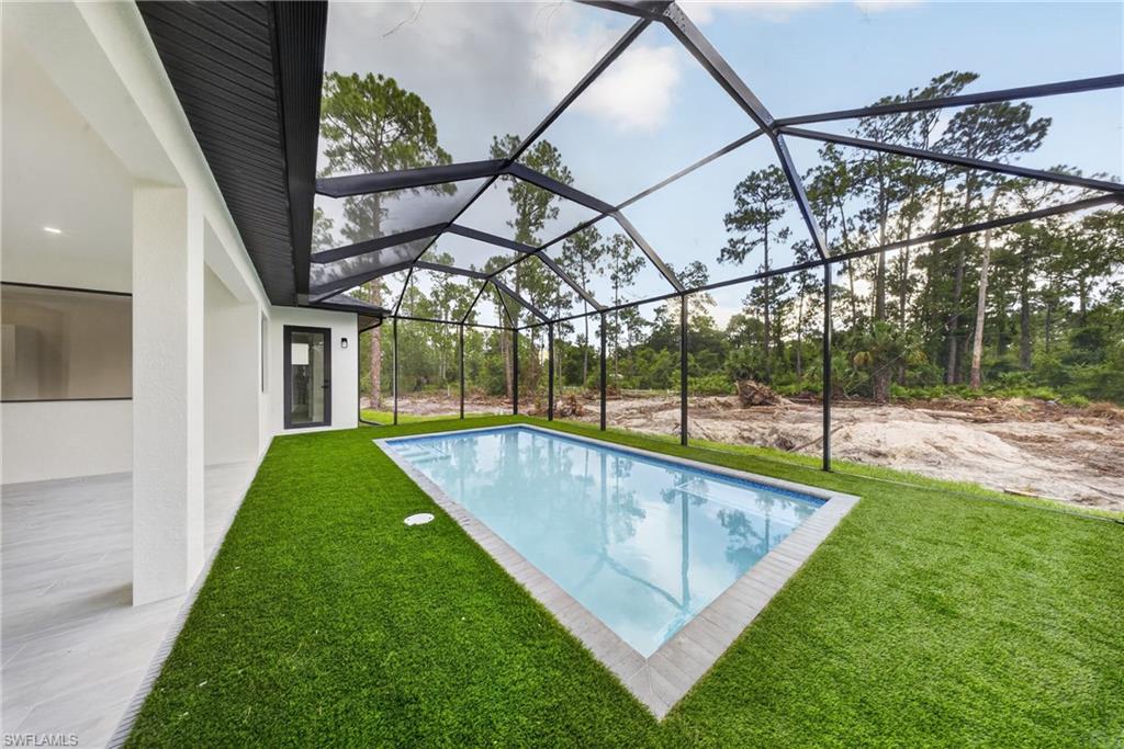Screened-in rectangular swimming pool featuring a grey tile surround and artificial turf decking