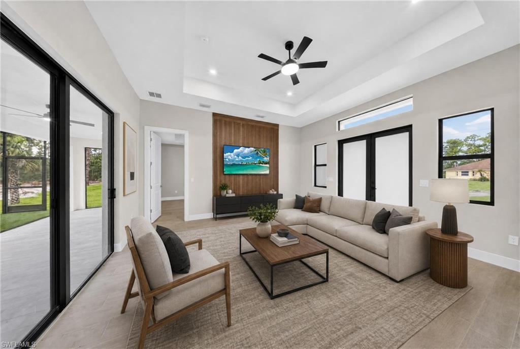Spacious living area featuring a tray ceiling with recessed lighting and a ceiling fan, a wood-paneled accent wall, large sliding glass doors, double French doors, and transom windows