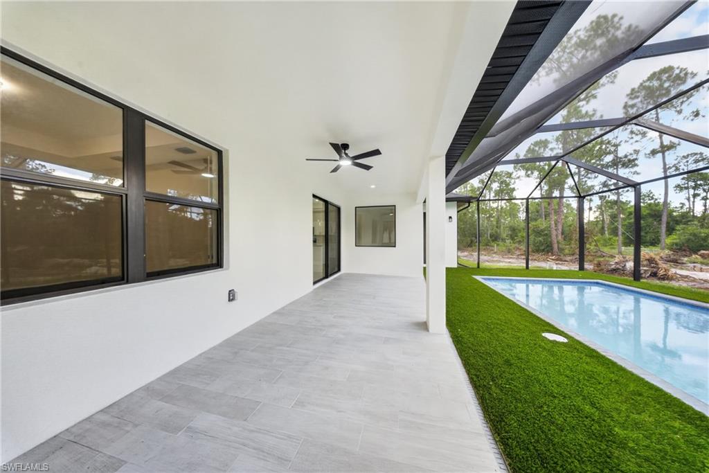 Expansive screened lanai featuring a rectangular swimming pool, artificial turf surround, and tiled flooring