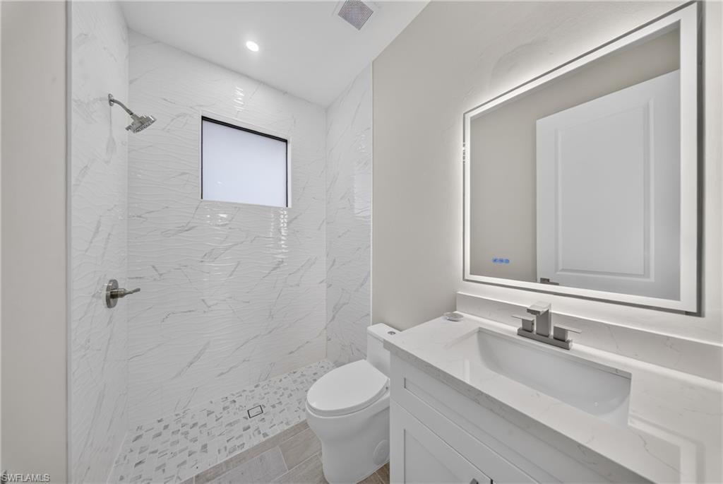 Contemporary bathroom featuring a walk-in shower with white marbled tile walls and a pebble-tiled floor