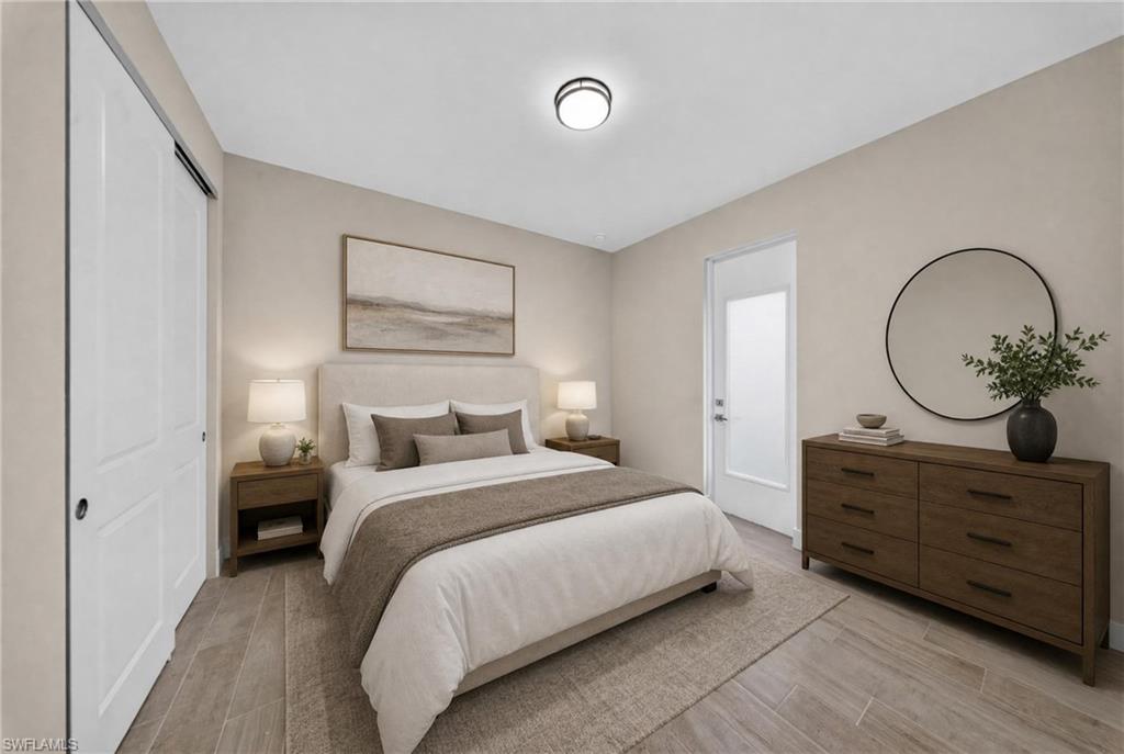 Spacious bedroom featuring wood-finish flooring, a contemporary ceiling light fixture, and a white paneled door with frosted glass