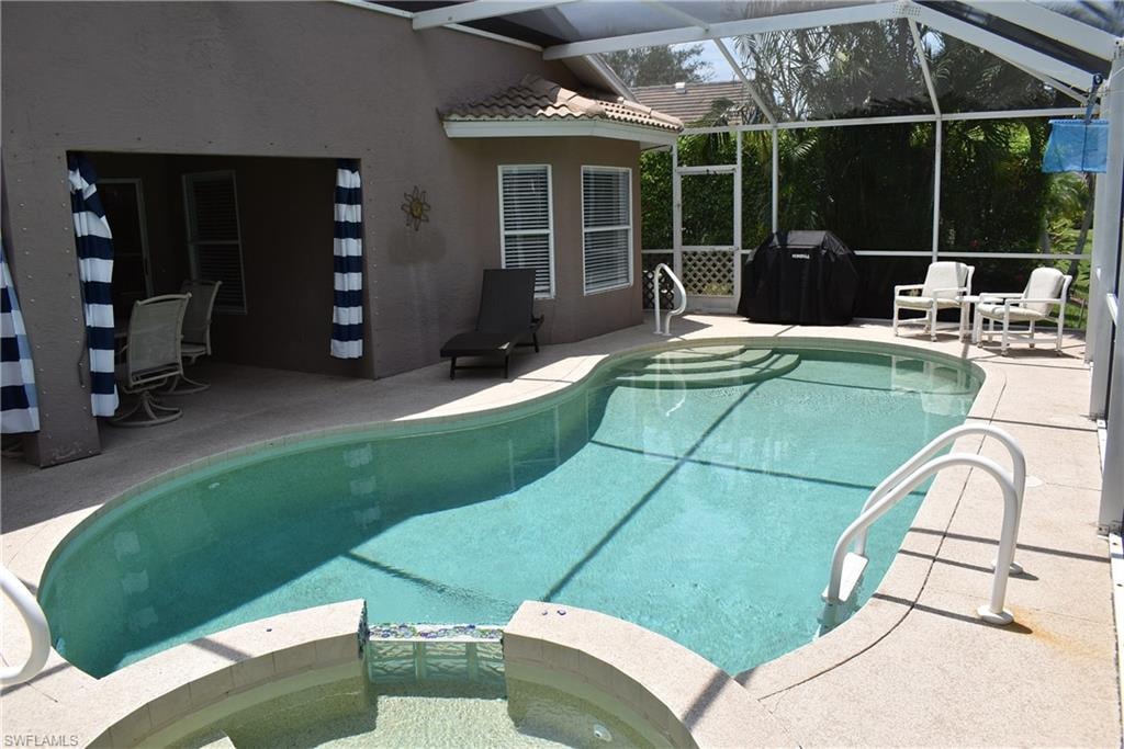 View of pool with glass enclosure, a patio area, an in ground hot tub, and grilling area