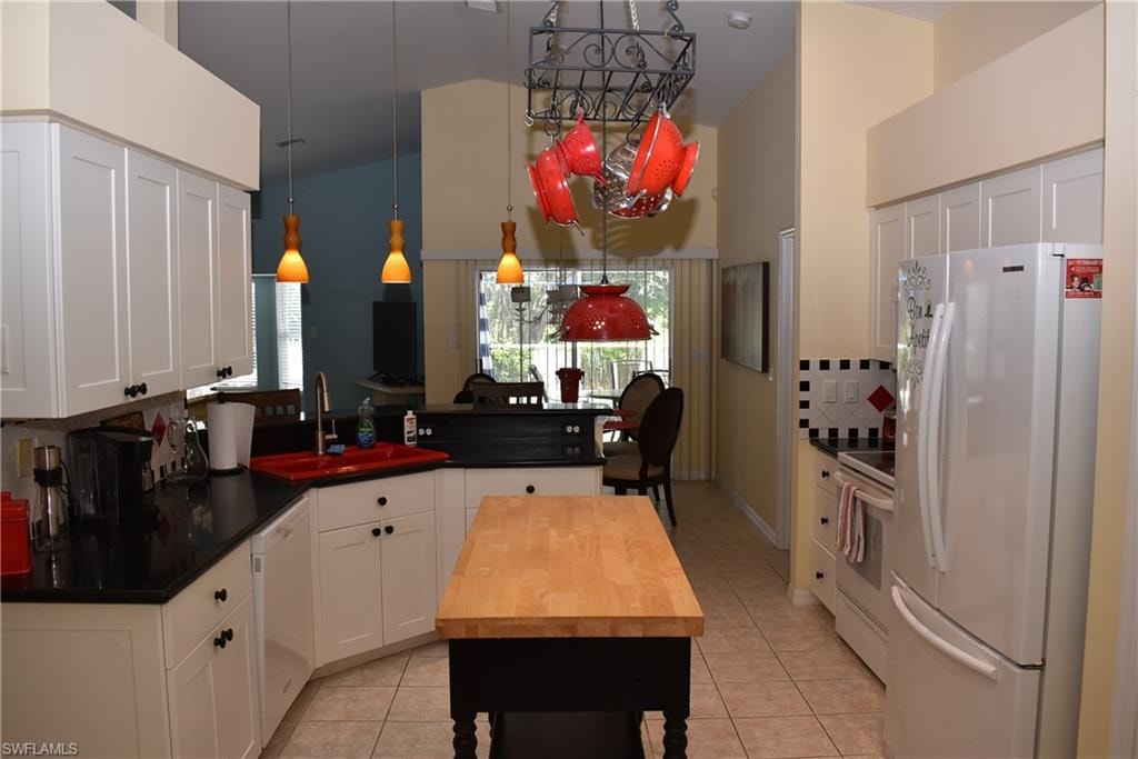 Kitchen with white appliances, sink, decorative light fixtures, light tile patterned flooring, and white cabinetry