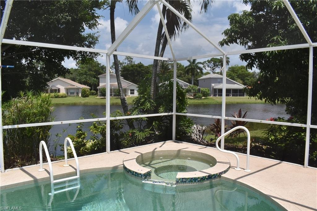 View of swimming pool with an in ground hot tub, a water view, and glass enclosure