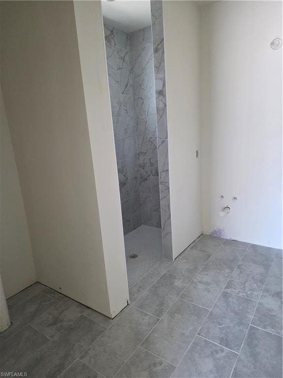 Spacious bathroom featuring large format gray tile flooring, a walk-in shower with natural stone-look wall tiling, and a coordinated tile shower pan