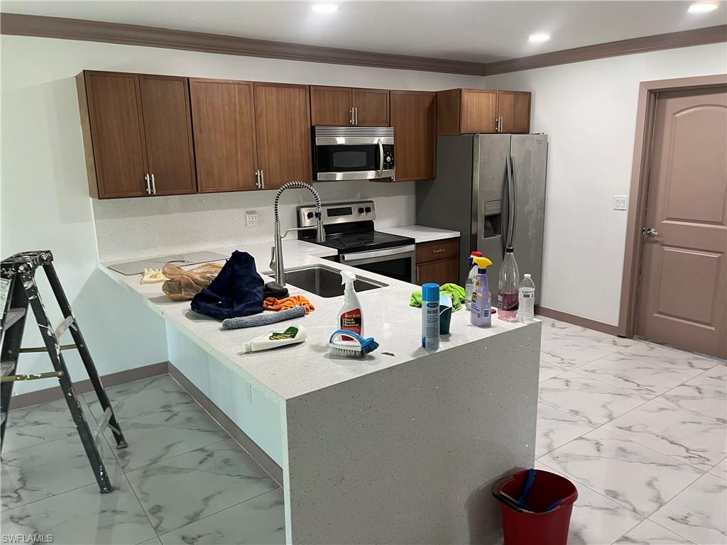 Kitchen with kitchen peninsula, sink, ornamental molding, and appliances with stainless steel finishes