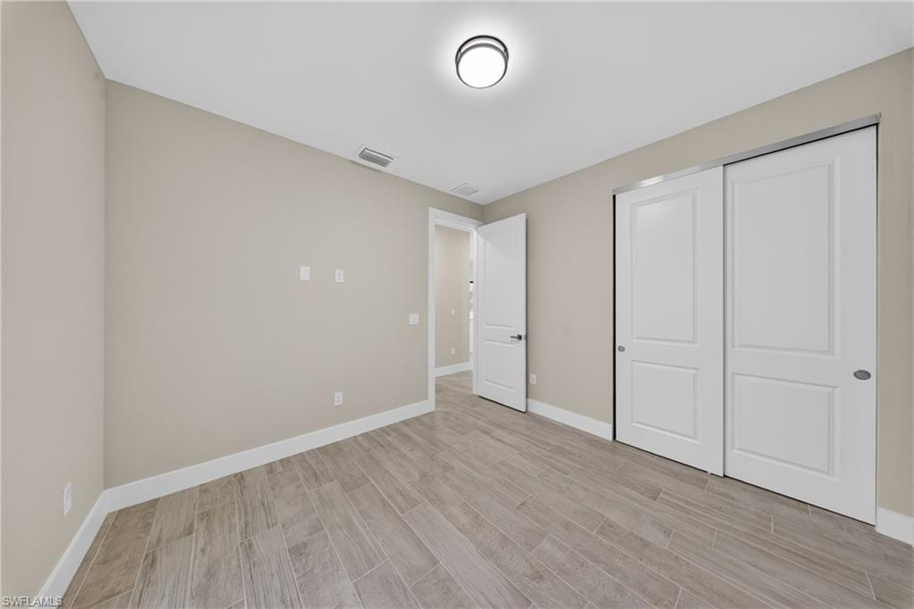 Room featuring light-toned walls, wood-look plank flooring, a flush-mount ceiling light fixture, and a sliding two-panel closet door