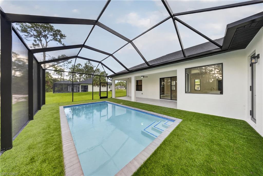 Screened-in pool area featuring a rectangular pool with integrated steps, artificial turf surround, and a covered patio