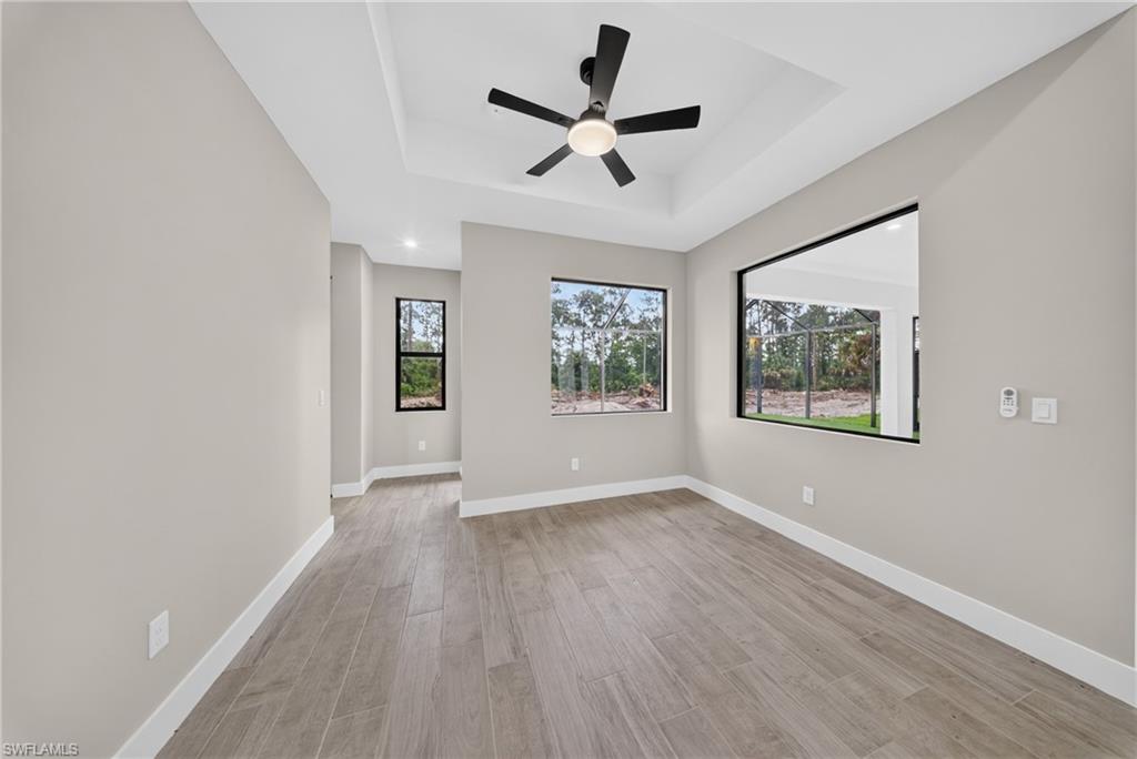 Spacious room featuring a tray ceiling with a ceiling fan, wood-finish flooring, and multiple large windows with black frames