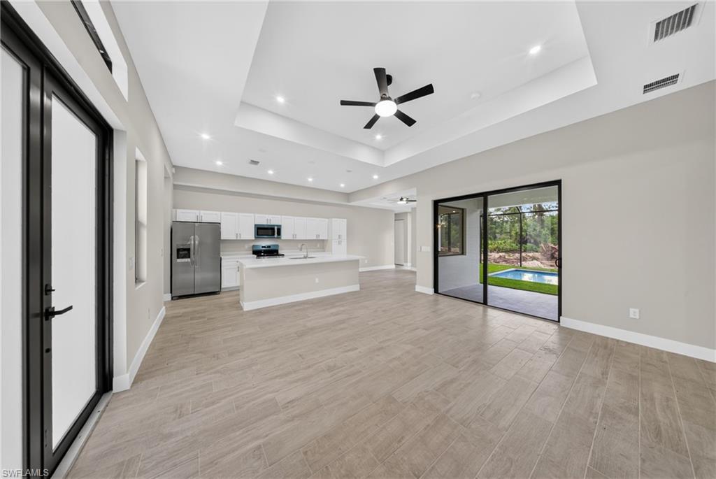 Open-concept kitchen and living area featuring wood-finish flooring, a tray ceiling with recessed lighting, a modern ceiling fan, and sliding glass doors leading to a screened outdoor area with a pool