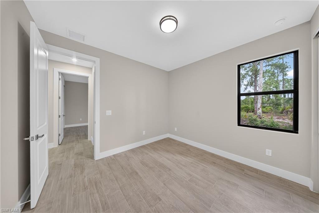Neutral-toned room featuring wood-finish flooring, white baseboards, and a single window with black trim