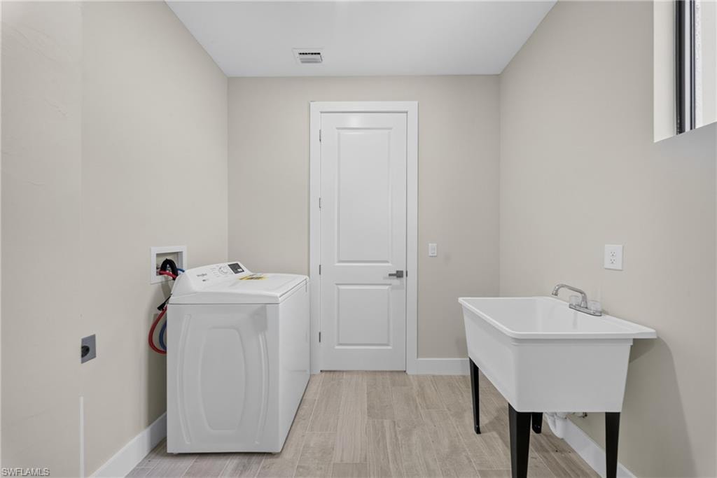 Dedicated laundry room featuring light wood-finish flooring, a utility sink with dual-handle faucet, and light neutral wall tones