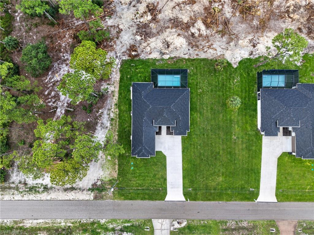 Aerial perspective showcasing a single-story residence with a dark shingle roof, an attached screened pool enclosure, and a concrete driveway