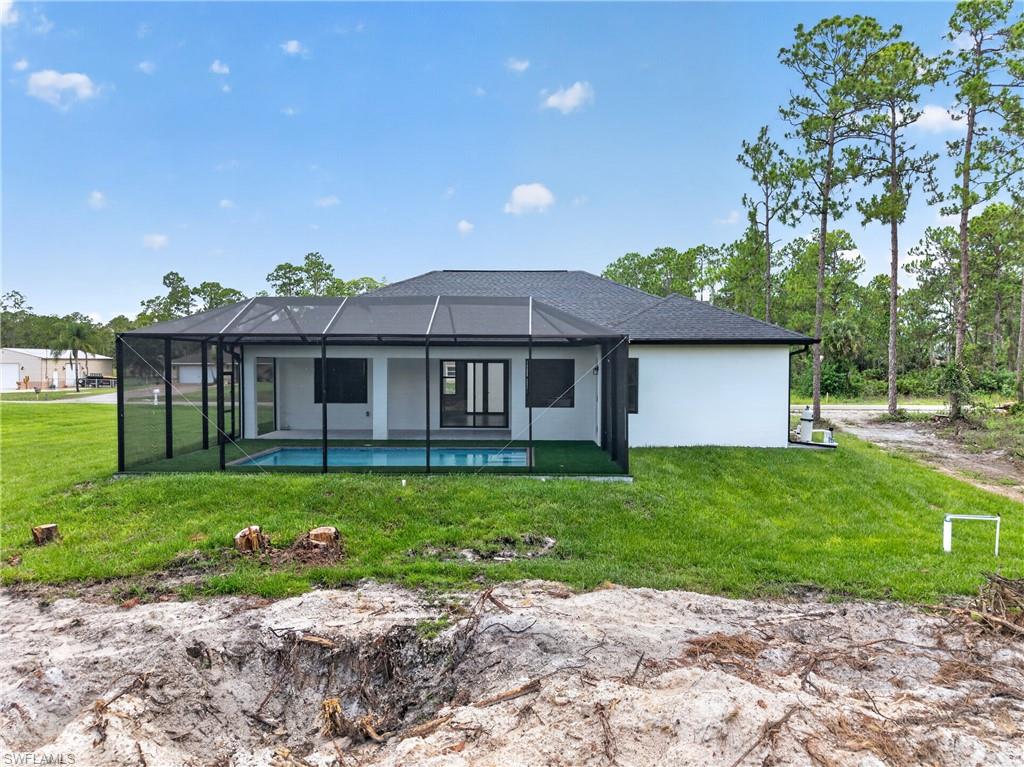 Rear exterior featuring a screened-in swimming pool enclosure, white stucco finish, and a dark shingle roof