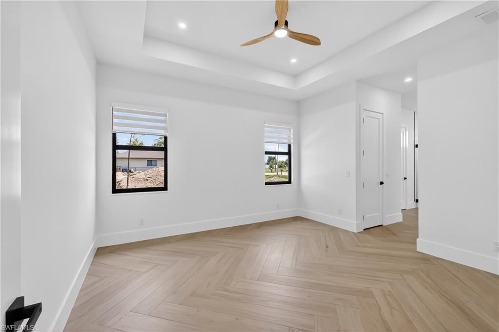 Spacious interior room featuring wood-finish herringbone flooring, a tray ceiling with recessed lighting, and a contemporary ceiling fan