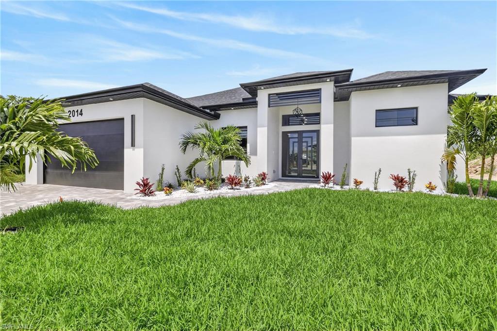 Modern exterior featuring a prominent covered entry with double doors, white stucco finish, dark trim accents, and a two-car garage